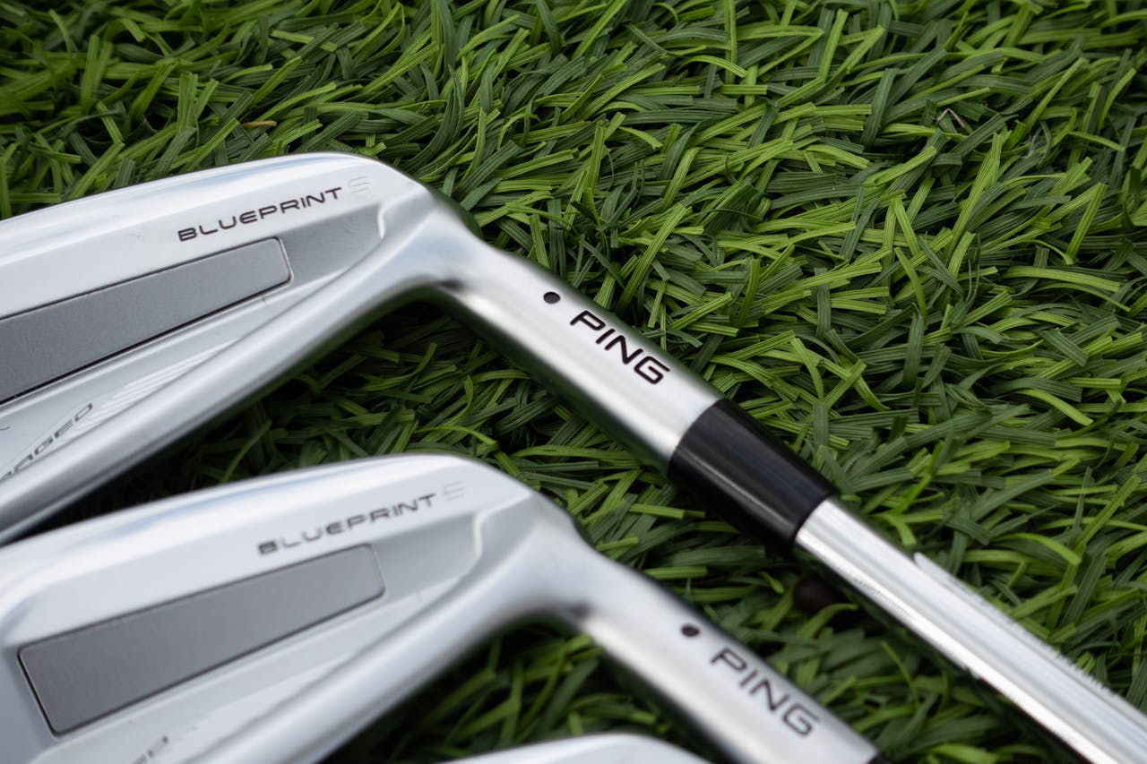 Detailed view of silver golf clubs resting on lush green grass, perfect for sports enthusiasts.